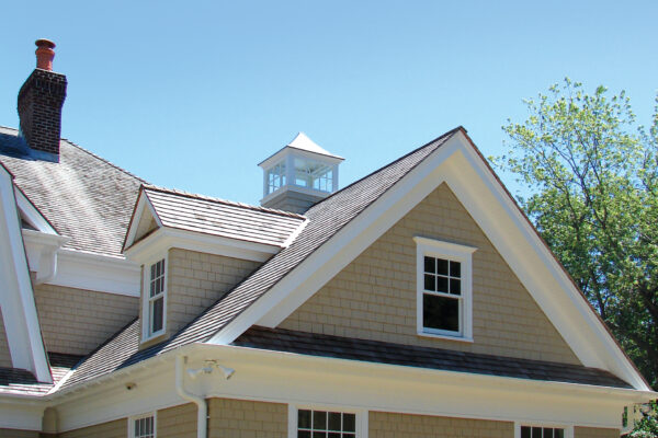 Beachgrass solid color prefinished cedar shingle siding on a gable-front home with bright white trim, a dark shingle roof, and a two-car garage.