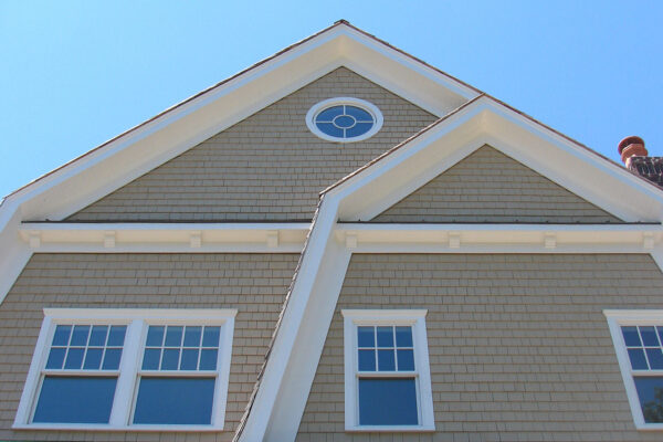 Beachgrass solid color prefinished cedar shingle siding on a gable-front home with bright white trim, an oval gable window, and a white balcony railing.