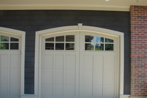 Burnt Hickory solid color prefinished cedar shingle siding above an arched white double garage door with window panels and white trim.
