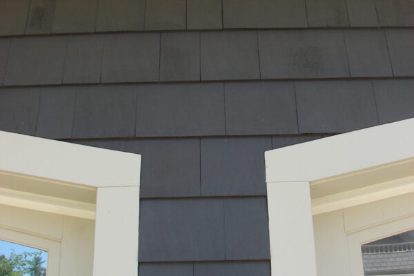 Burnt Hickory solid color prefinished cedar shingle siding on a two-story home with white trim, white porch columns, and a dark front door.