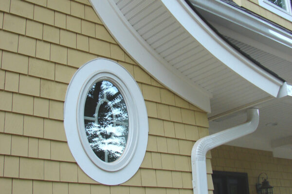 Colonial Yellow solid color prefinished cedar shingle siding installed on a home exterior with white trim and an oval window.