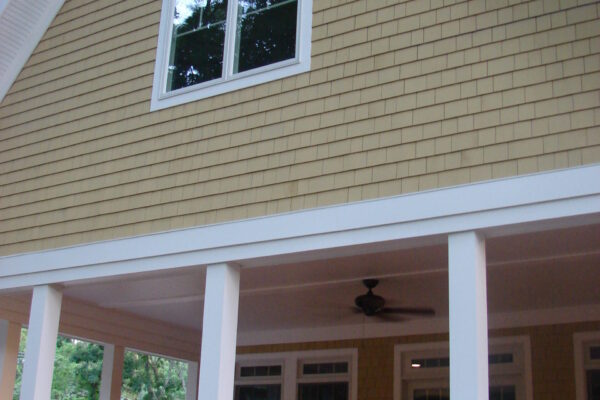 Colonial Yellow solid color prefinished cedar shingle siding on a gable wall with white trim and an arched-top window above a covered porch.