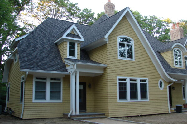 Colonial Yellow solid color prefinished cedar shingle siding on a front porch wall with white trim, black shutters, and a black lantern beside a window.
