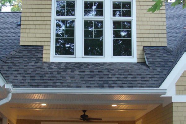 Colonial Yellow solid color prefinished cedar shingle siding on a two-story home with white trim, black shutters, and a covered porch.
