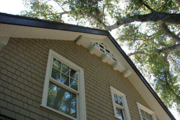 Dune Gray solid color prefinished cedar shingle siding on a cottage-style home with white trim, a covered porch, and a dark shingle roof.