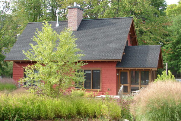 Flint Corn solid color prefinished cedar shingle siding on a gable-front cottage with natural wood trim and a screened porch.