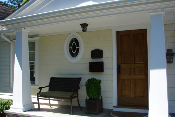 Linen solid color prefinished cedar shingle siding on a two-story home with white trim, black shutters, and a red front door.