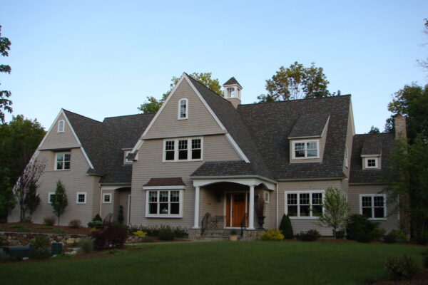 Seacoast Gray solid color prefinished cedar shingle siding on a coastal home with white trim, a covered porch, and a light stone chimney.