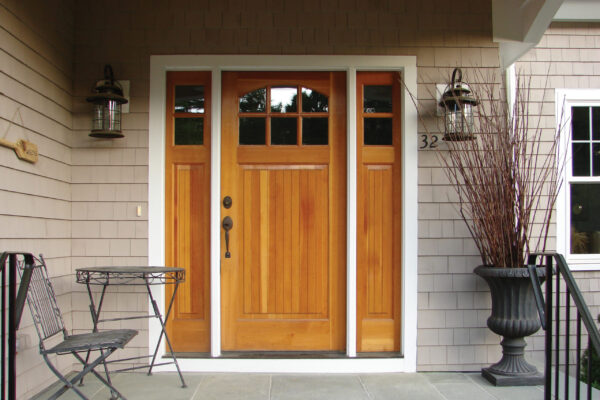 Seacoast Gray solid color prefinished cedar shingle siding on a covered front porch with white trim and a natural wood entry door with sidelights.
