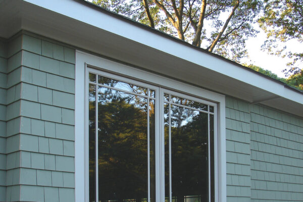 Sycamore solid color prefinished cedar shingle siding on a gable-front craftsman home with white trim, a stone foundation, and a covered porch.