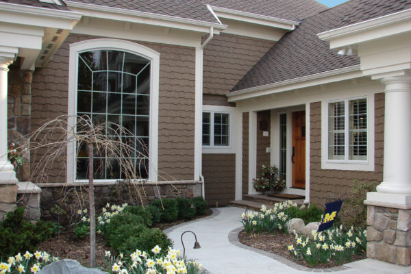 Taupe solid color prefinished cedar shingle siding on a front entry courtyard with white trim, stone wainscot, and a natural wood front door.