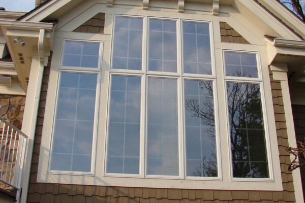 Taupe solid color prefinished cedar shingle siding on a gable wall with large white-trim windows and a white louvered gable vent.