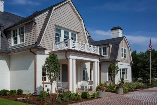 Front exterior of a home with light gray cedar shingle siding, white trim, and a covered porch with white columns and a second-story balcony.