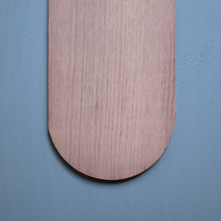 Round Close-up of a cedar shingle with a rounded butt edge, shown as a single wood piece against a blue background.