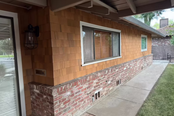 natural-cedar-shingle-siding-brick-wainscot-white-trim-exterior-wall Exterior wall with natural cedar shingle siding above a red brick wainscot, featuring white-trim windows and a covered soffit overhang.