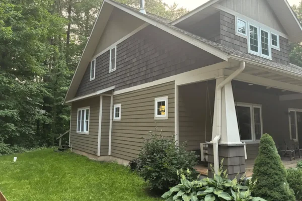 Gray cedar shingle siding on the upper story of a gable-roof house above tan lap siding, with white trim and a covered porch.